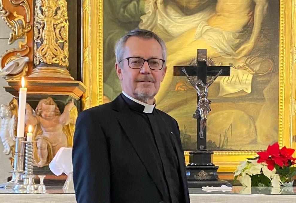 Prästen Anders Lindström står framför altaret. Till höger om honom pryds altaret av ett krusifix och en blomma, en julstjärna, och till vänster på altaret står två tända ljus.
