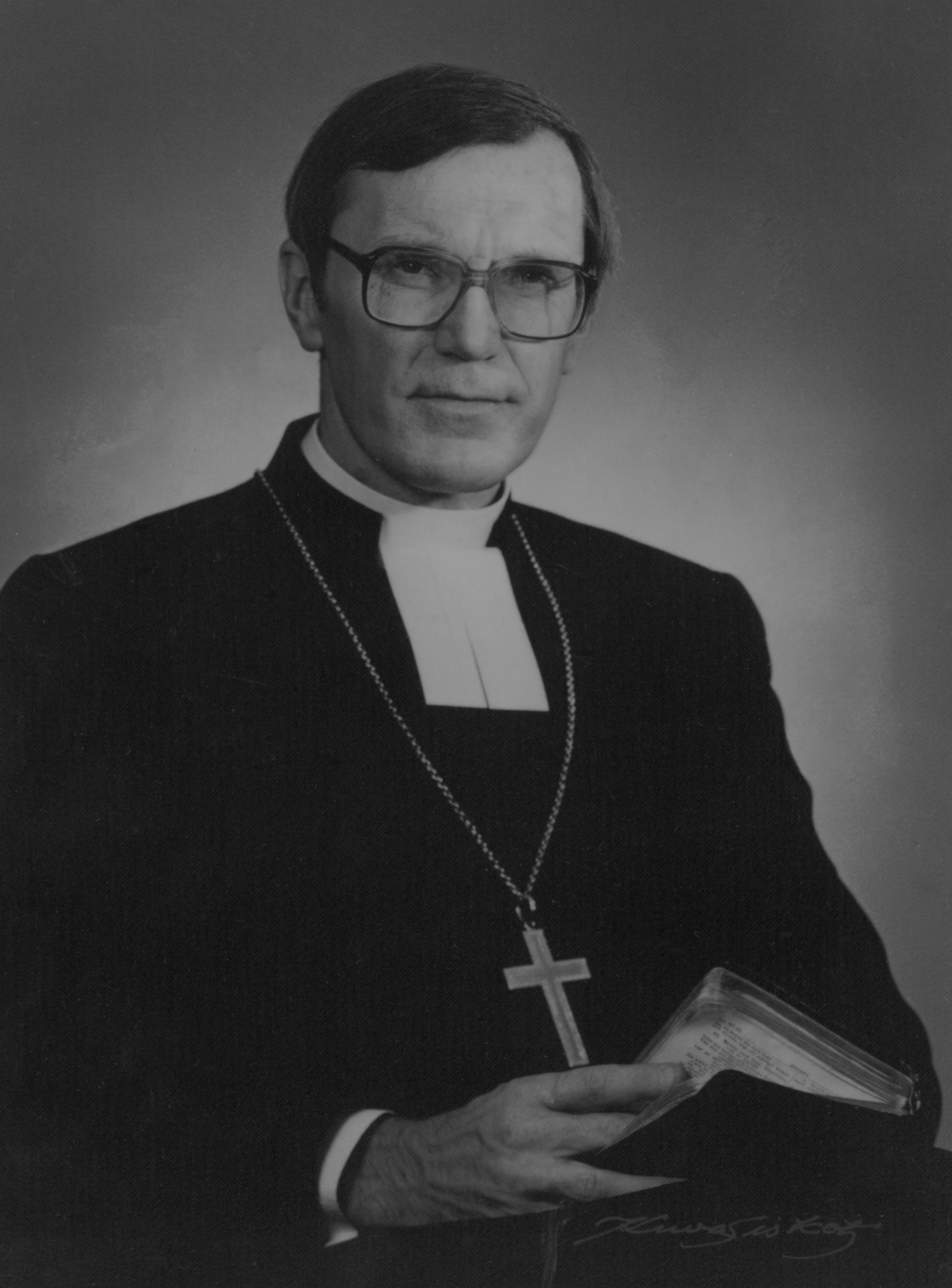 Mörkhårig Erik Vikström med glasögon iklädd kaftan och biskopskors och med Bibeln i hand.