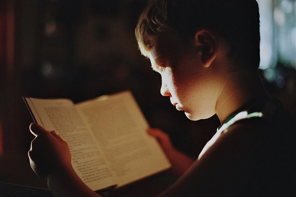Poika lukee hämärässä valossa kirjaa.
