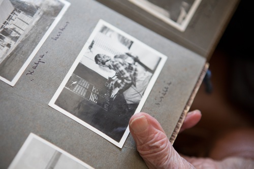 Lähikuva mustavalkoisista valokuvista vanhassa valokuva-albumissa, jota pitelee vanhan ihmisen käsi.