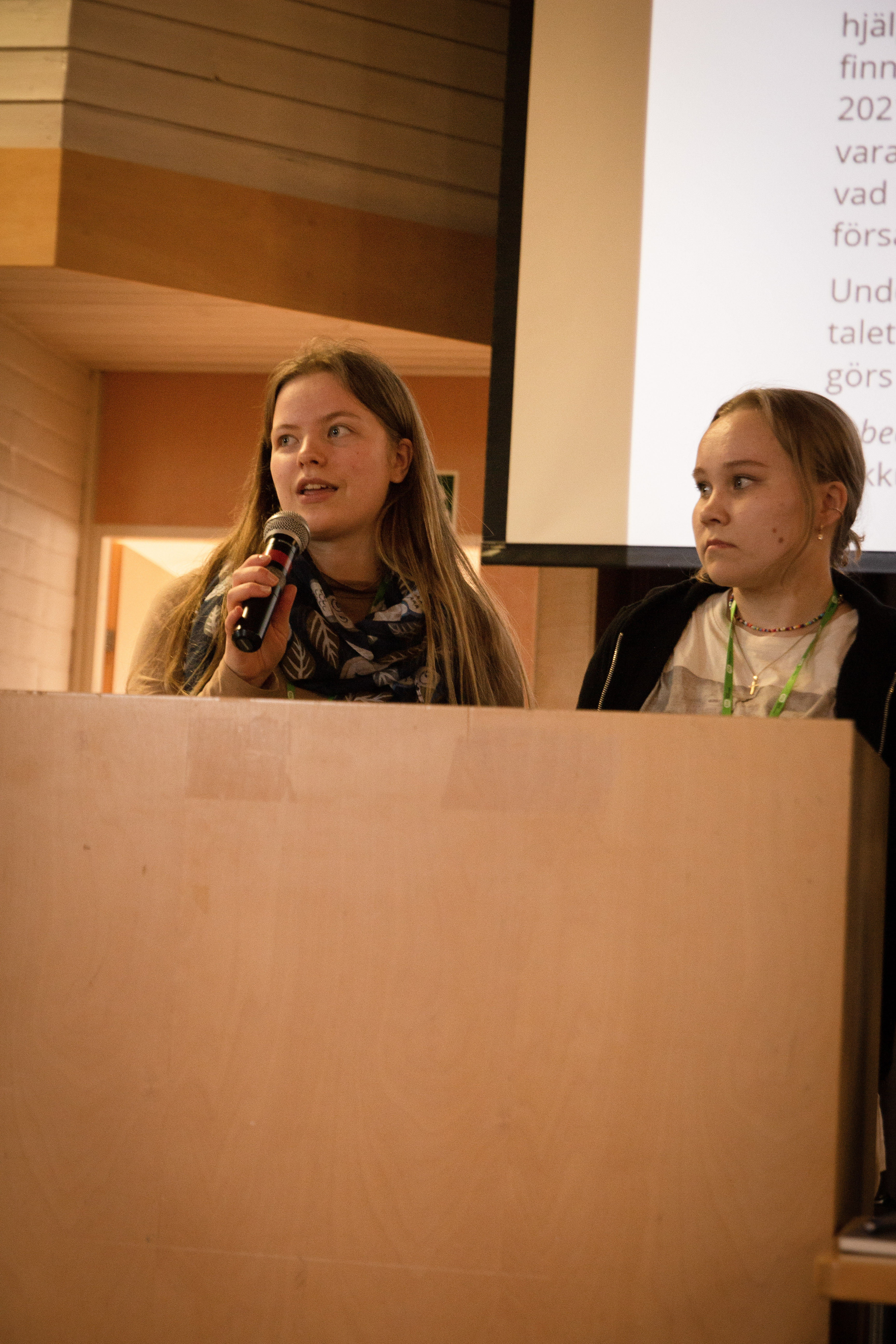 Två unga kvinnor i talarstol presenterar text på skärm.