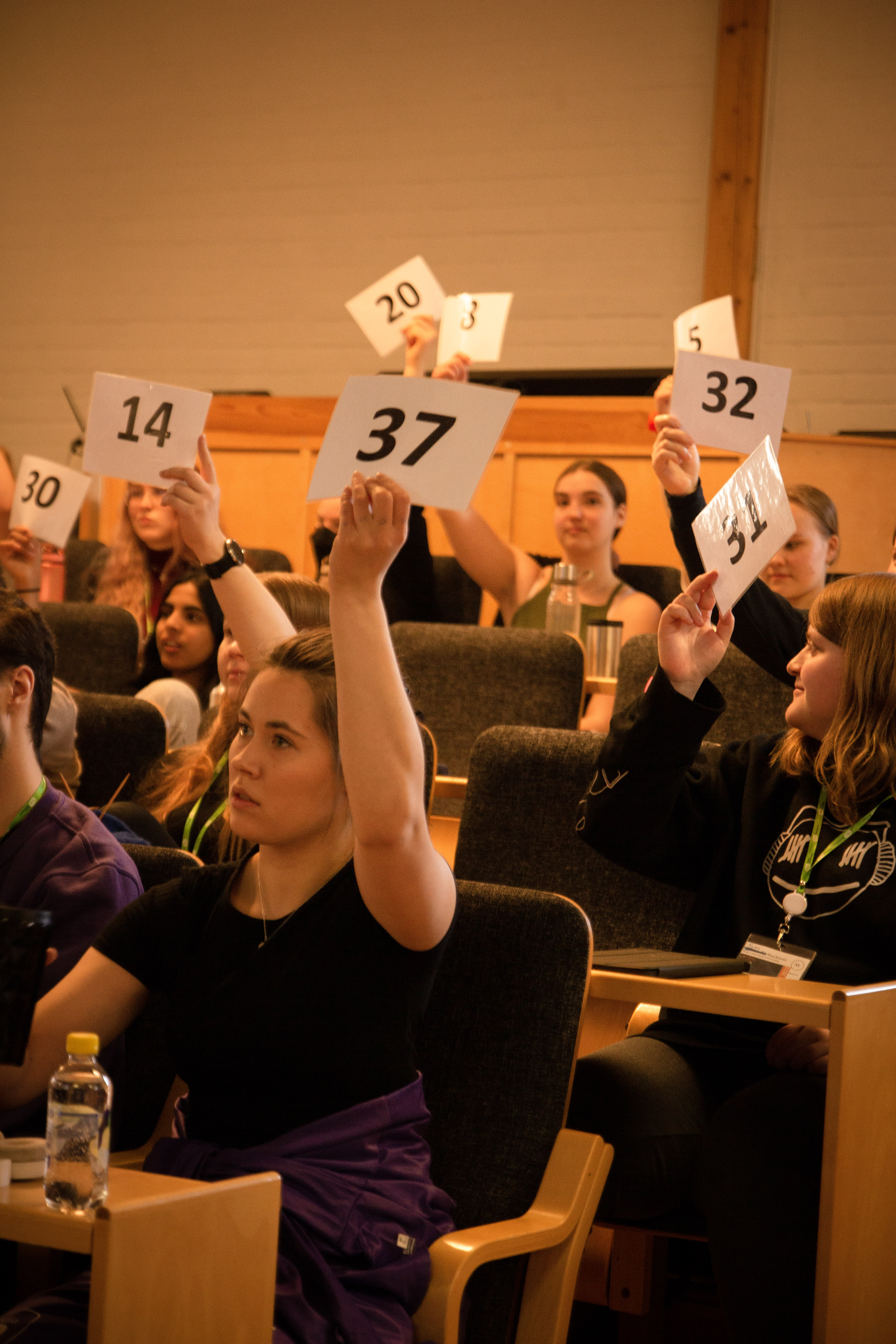 Ungdomar i auditorium håller upp kort med siffror på.