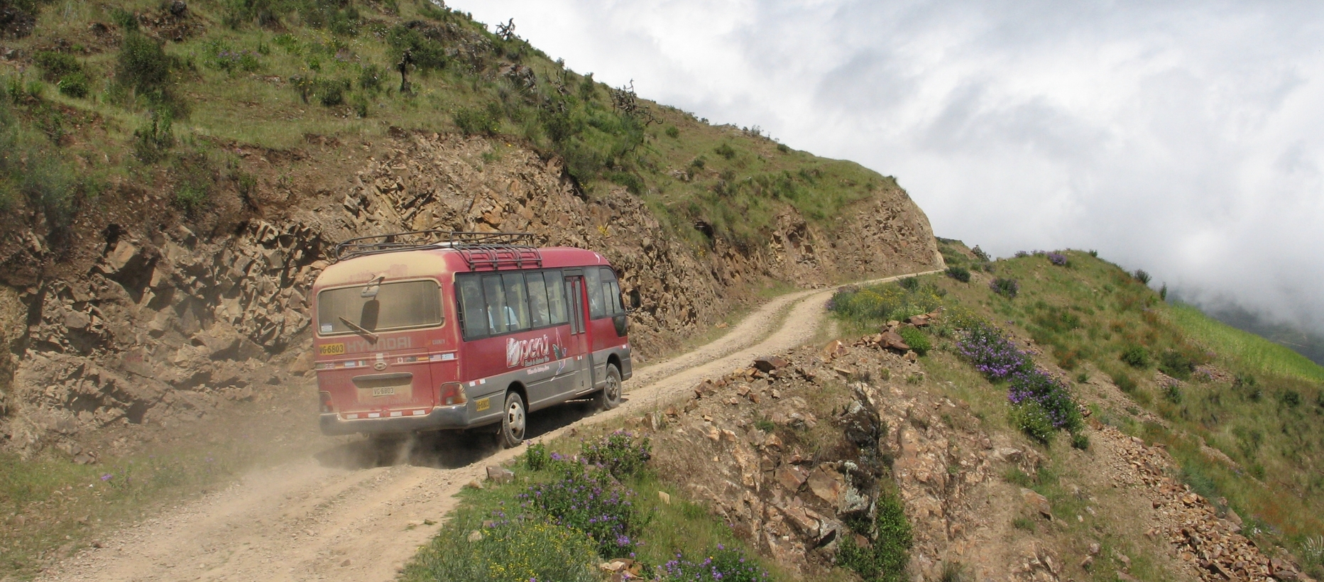 En gammal buss kör på en dammig bergsväg.
