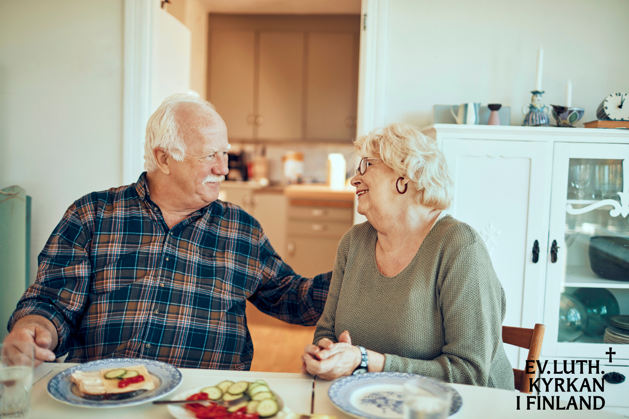 Ett äldre par sitter vid matbordet och ler mot varandra.