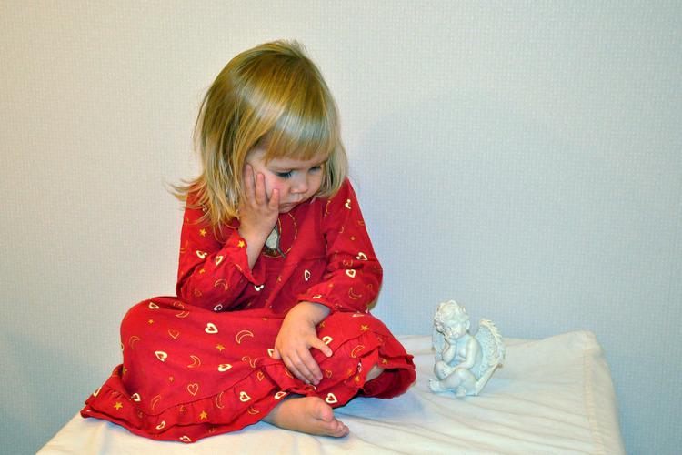 Flicka som lutar huvudet i handen på samma sätt som en porslinsängel som hon sitter bredvid