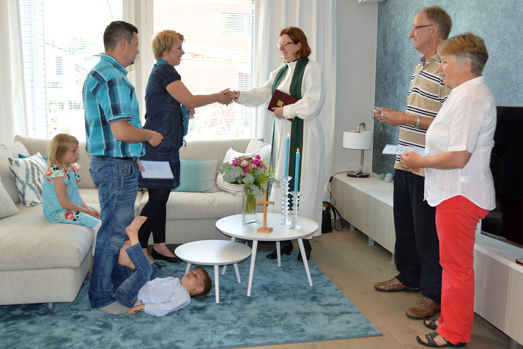 Prästen och frun i huset skakar hand vid ett välsignelsetillfälle i hemmet