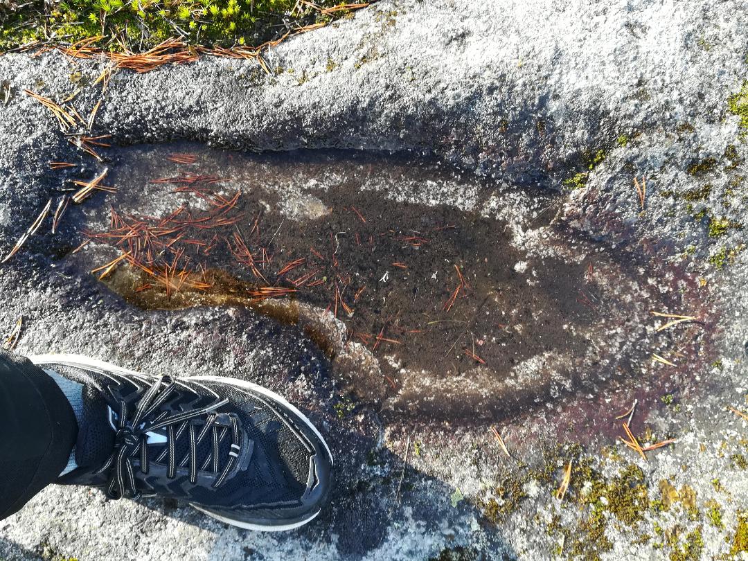 En fot brevid brevid en skålgrop i berget. Gropen i berget ser ut som en fot.