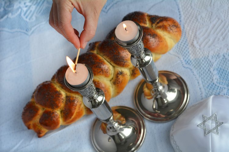 Kaksi kynttilää kynttilänjaloissa, challa-leipä ja kipa-päähine.