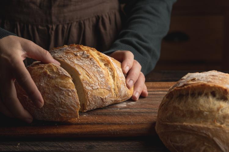 Händer delar ett nybakat bröd.