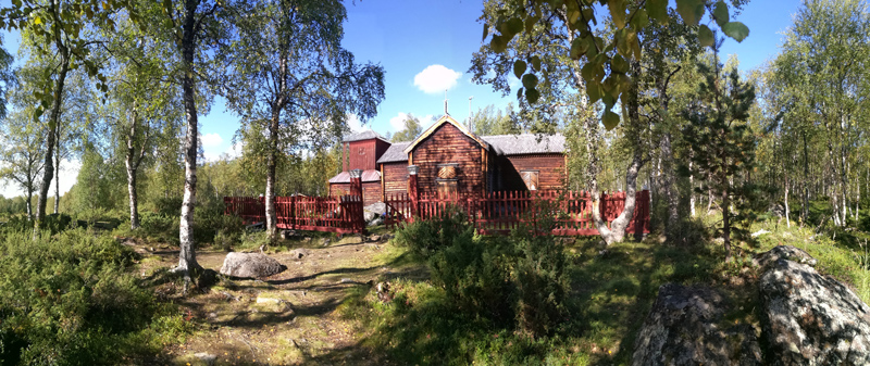 Punaruskea puukirkko luonnon keskellä.