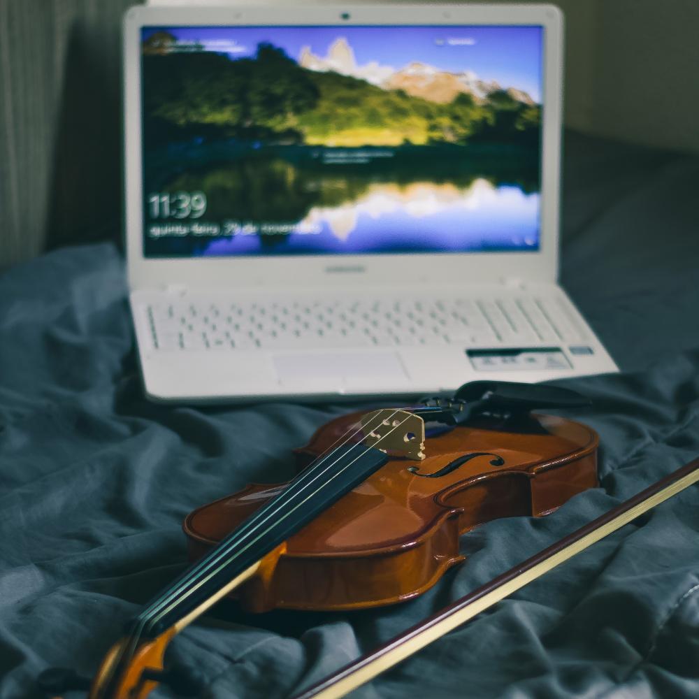 Dator och violin på en säng.