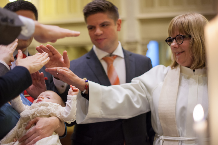Kummit, pappi ja vanhemmat siunaavat lapsen kasteen jälkeen.