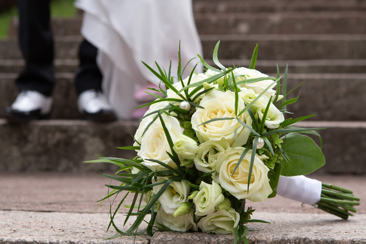 Valkoisista ruusuista tehty hääkimppu kirkon portailla.