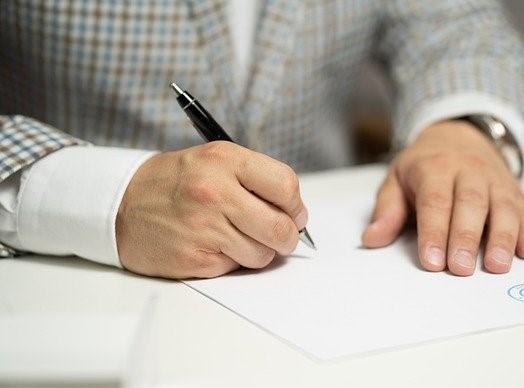 Händerna på en person som undertecknar dokument.