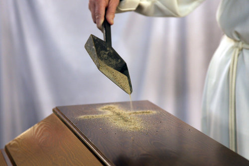 Pappi heittää ruumisarkun päälle hiekkaa ristin muotoon.
