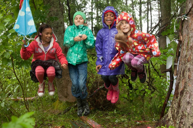 Tytöt hyppivät sateessa metsässä.