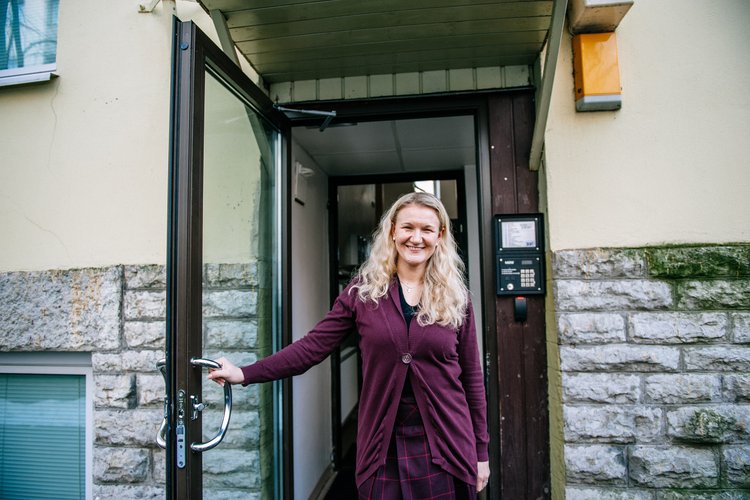 Hymyilevä nainen avaa kerrostalon porraskäytävän oven.