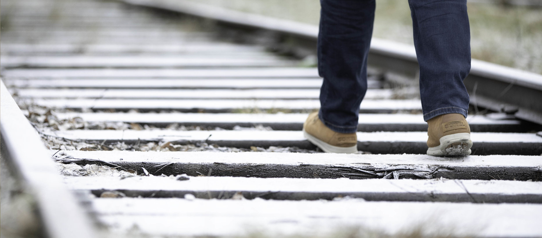 Rautatiekiskot, joilla kävelee ihminen, jolla on siniset farkut ja ruskeat kengät.