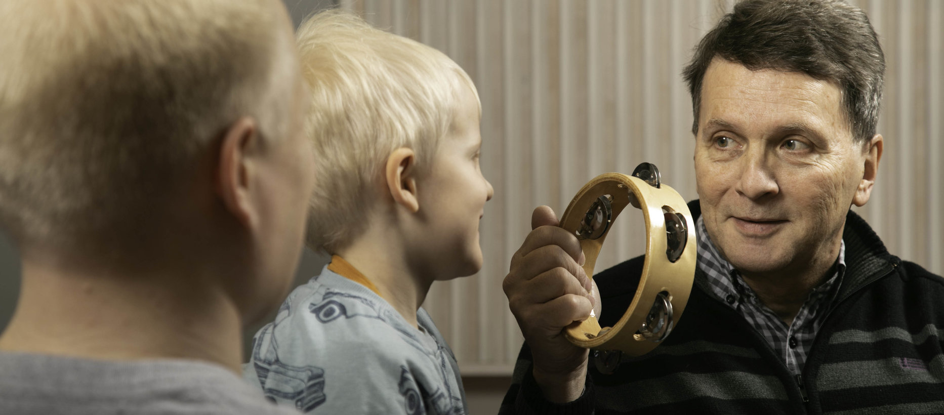 Lapsi ja kaksi aikuista soittavat tamburiinia.