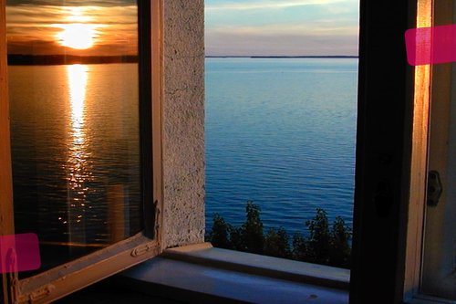 Auki oleva ikkuna. Tyyni merimaisema. Auringonlasku.