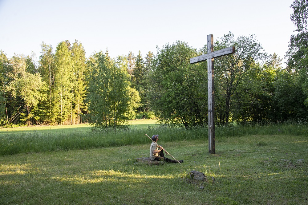 Ihminen istumassa maassa katsoen suurta puista ristiä Turun Ristinpellolla.