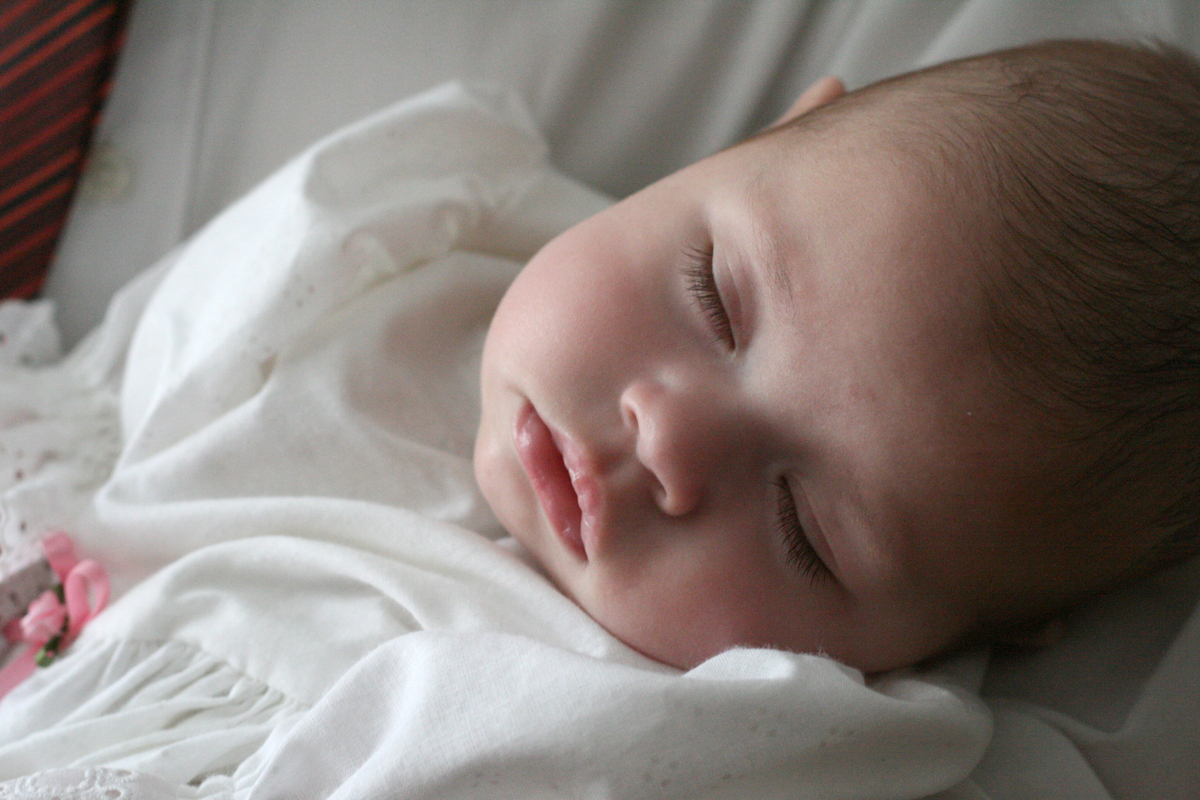 Sovande baby iklädd dopdräkt.