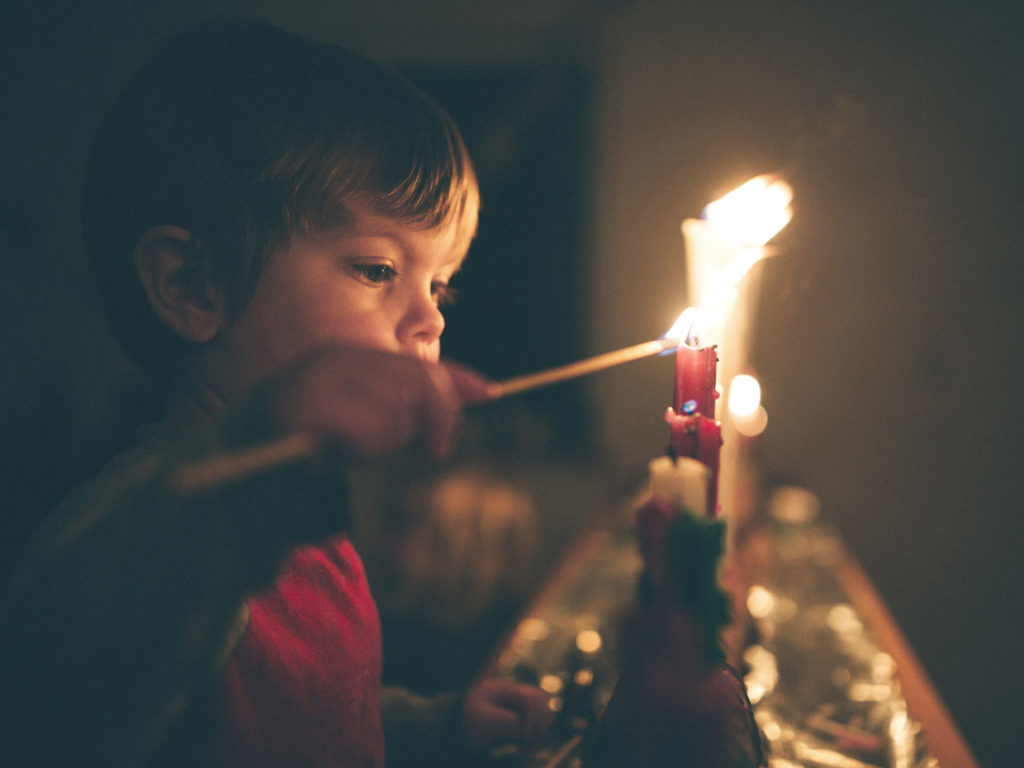 Kuvassa lapsi sytyttää kynttilöitä.