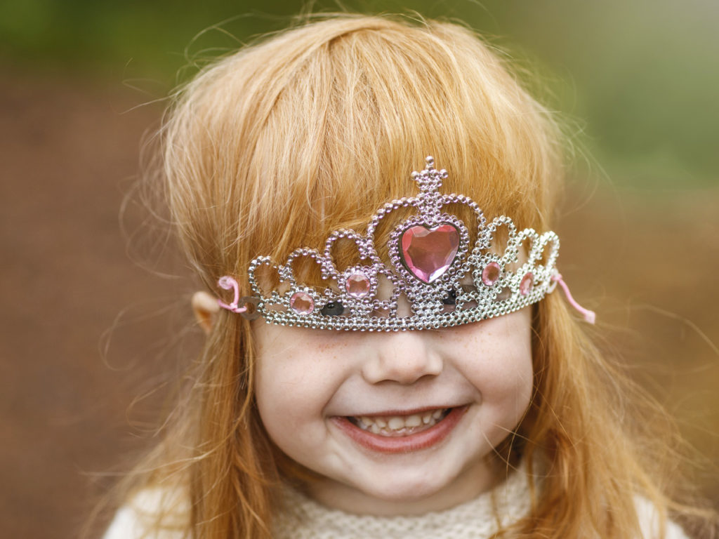 Kuvassa hymyilevä lapsi, jolla prinsessakruunu valahtanut silmille.