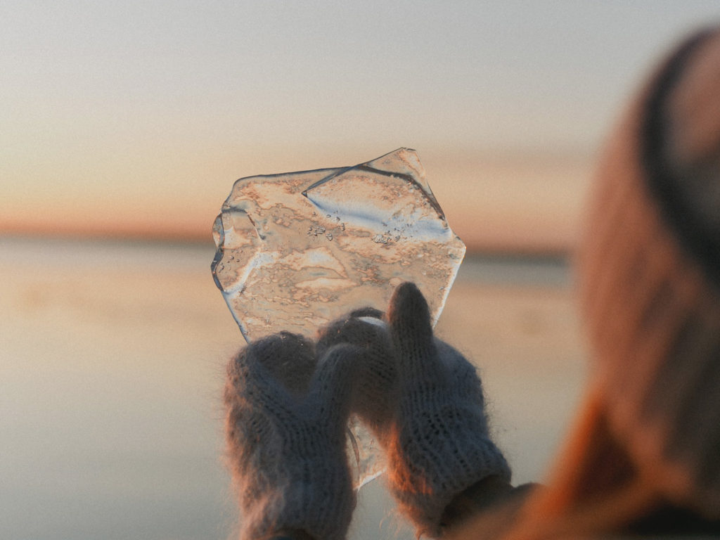 En människa håller i handen en isbit, i bakgrunden horisonten.