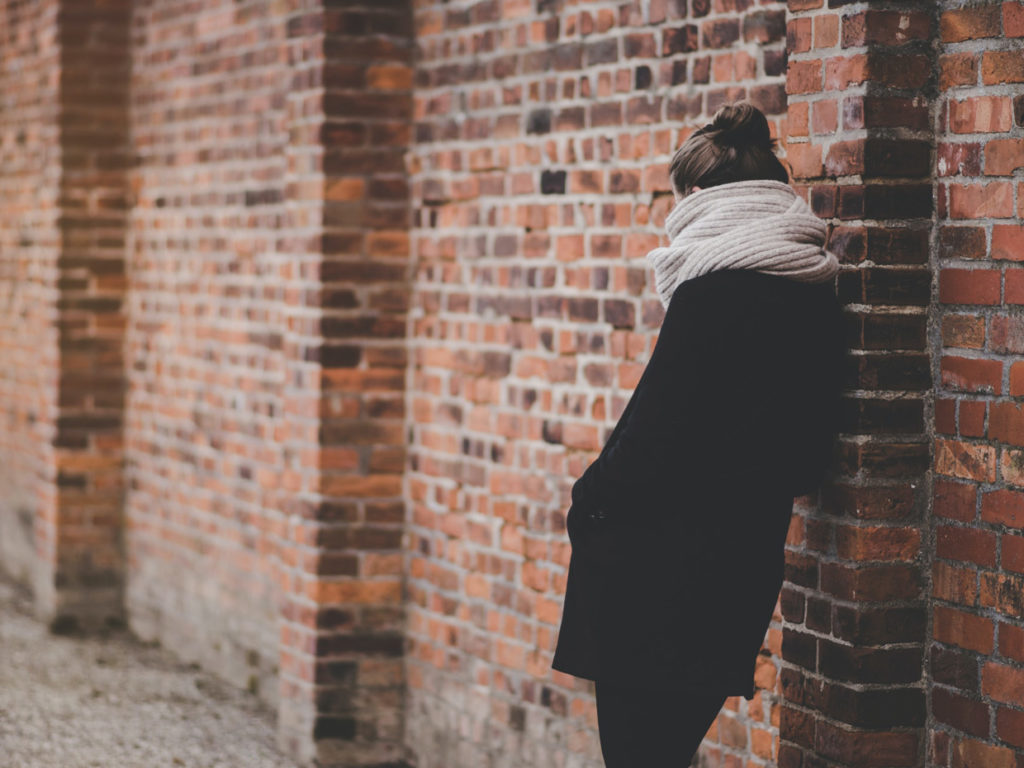 Ensam person som står lutad mot en vägg