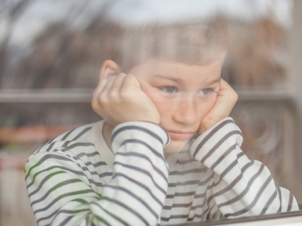 Ett barn sitter i fönstret hen lutar ansiktet i båda händerna.