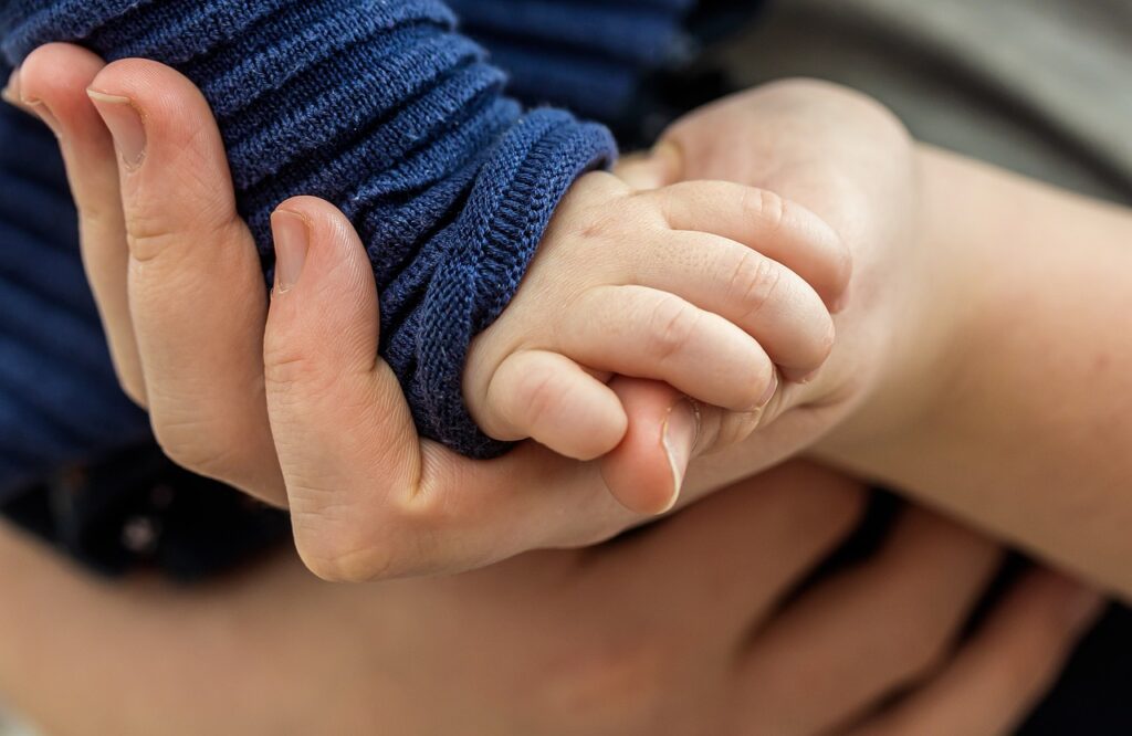 Kuvassa pienen lapsen käsi puristaa aikuisen peukaloa