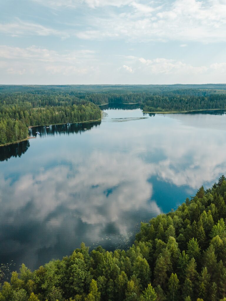Landskapsbild på insjö i vilken det speglas moln. Sjön är omgivern av skog.