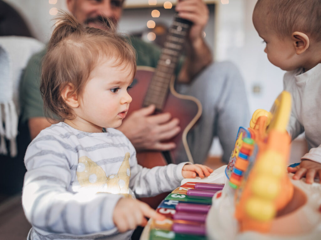 Barn leker med instrument, en man spelar gitarr.