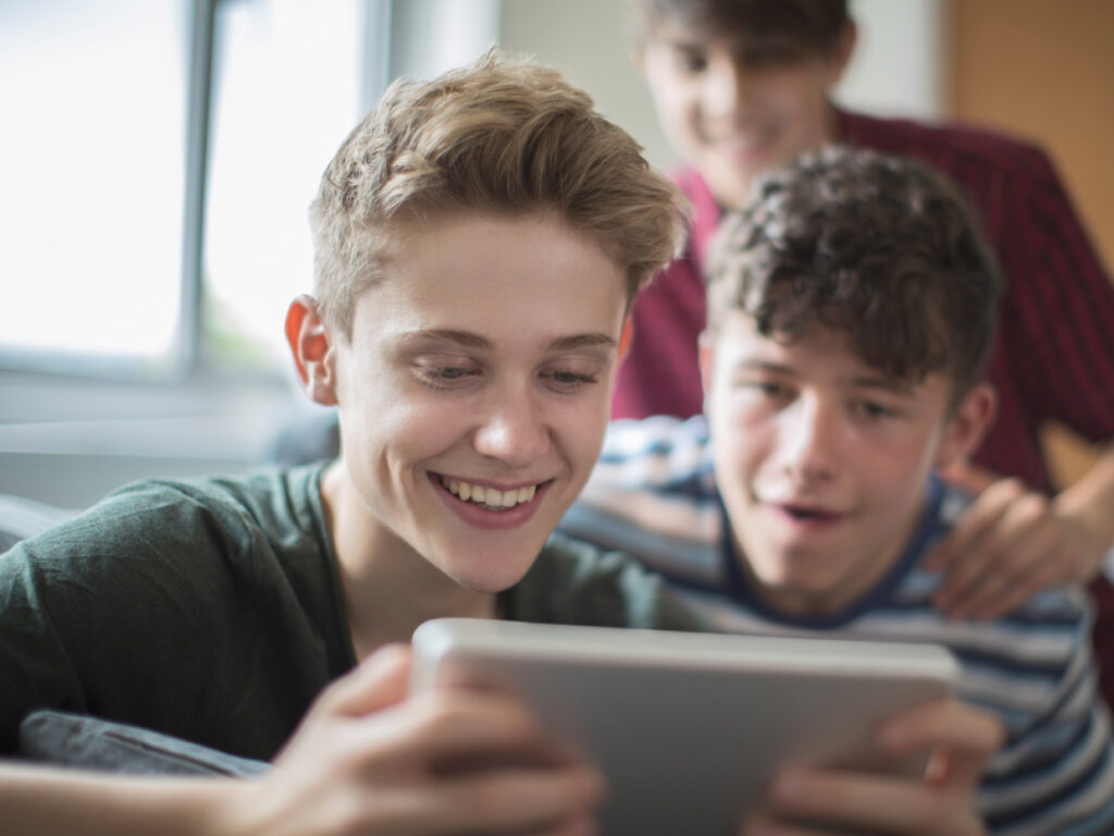 Tre tonårspojkar tittar tillsammans på en skärm.