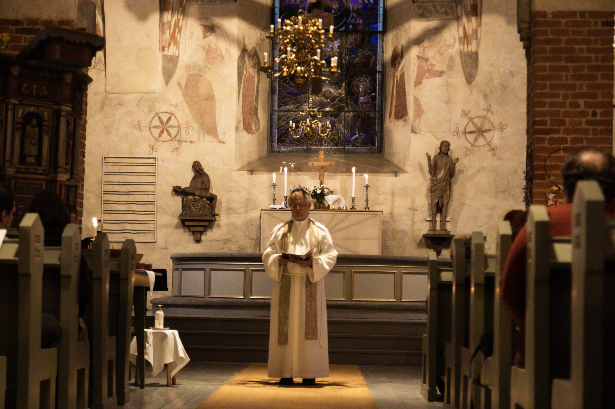 Präst står framme i en medeltida kyrka i mittgången och talar till församlingen.