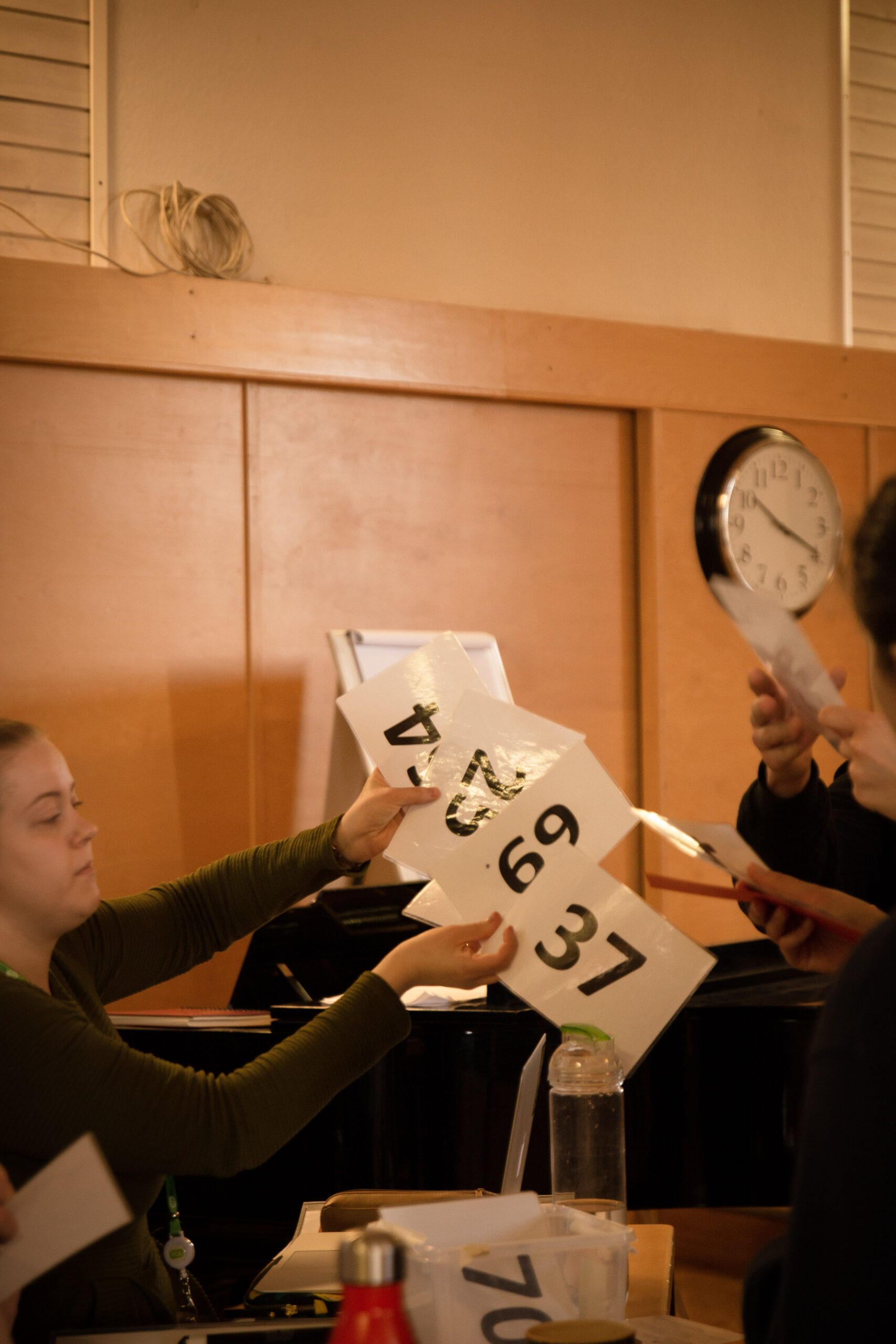Ung kvinna sitter bakom ett bord och delar ut sifferkort till ungdomar.