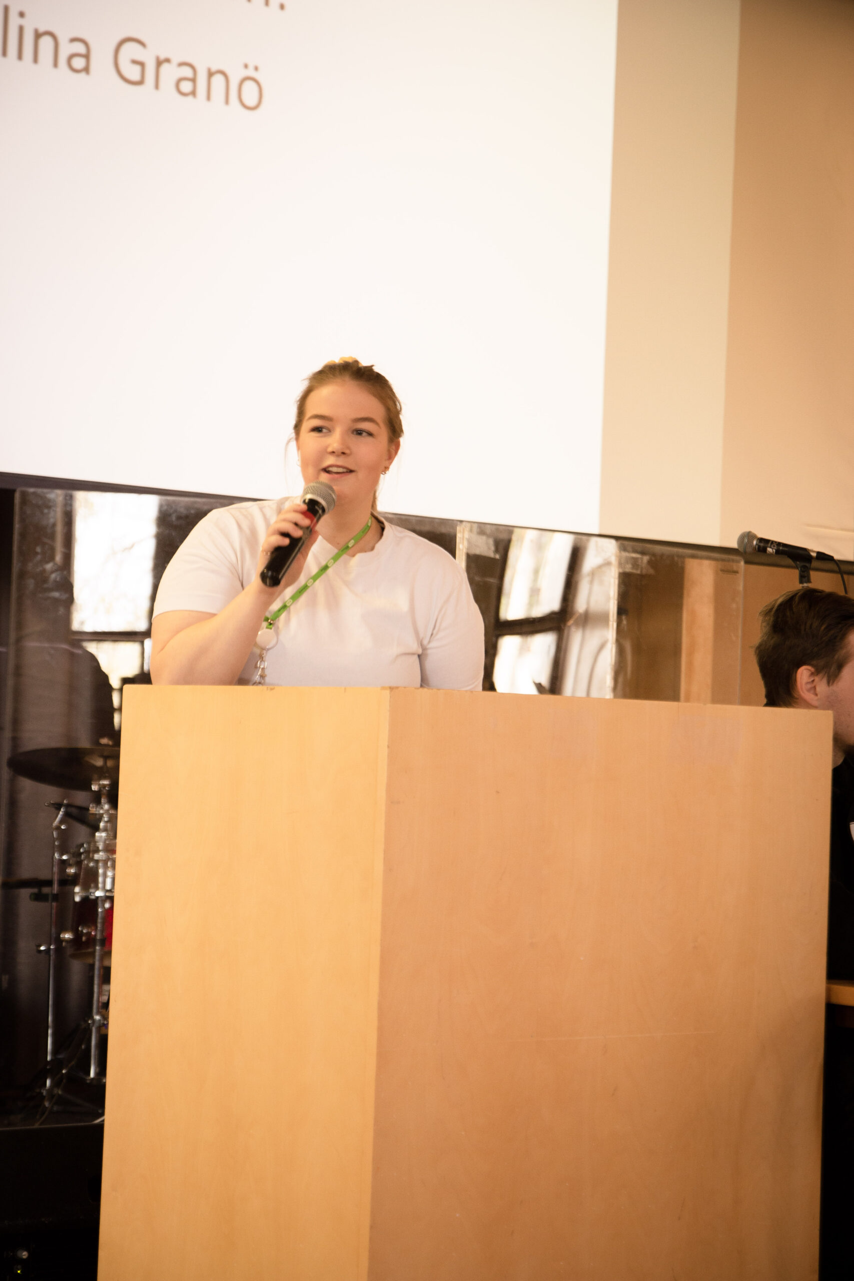 Ung kvinna med ljus skjorta talar i mikrofon från en talarstol.