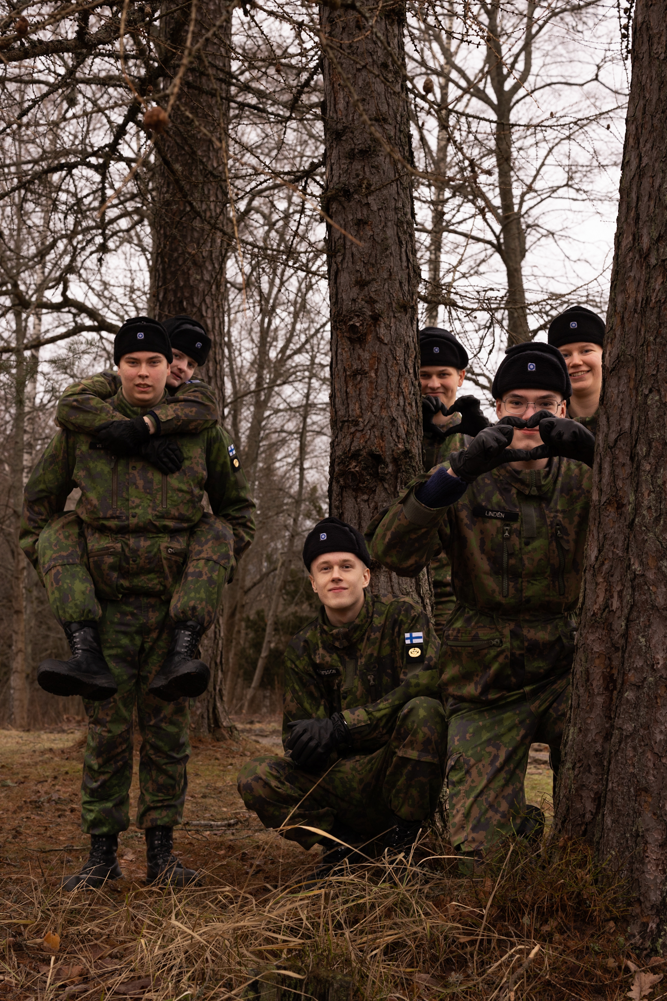 Sex unga militärtjänstgörare poserar bland träd.