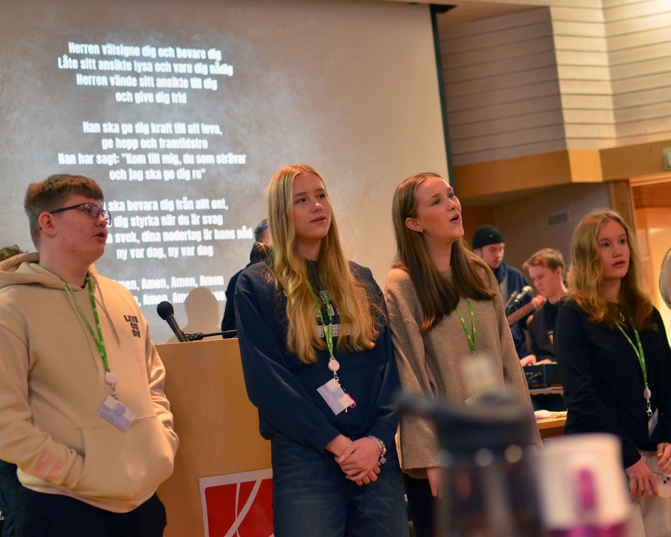 Fyra ungdomar står bredvid varandra framför en skärm som visar en sångtext.