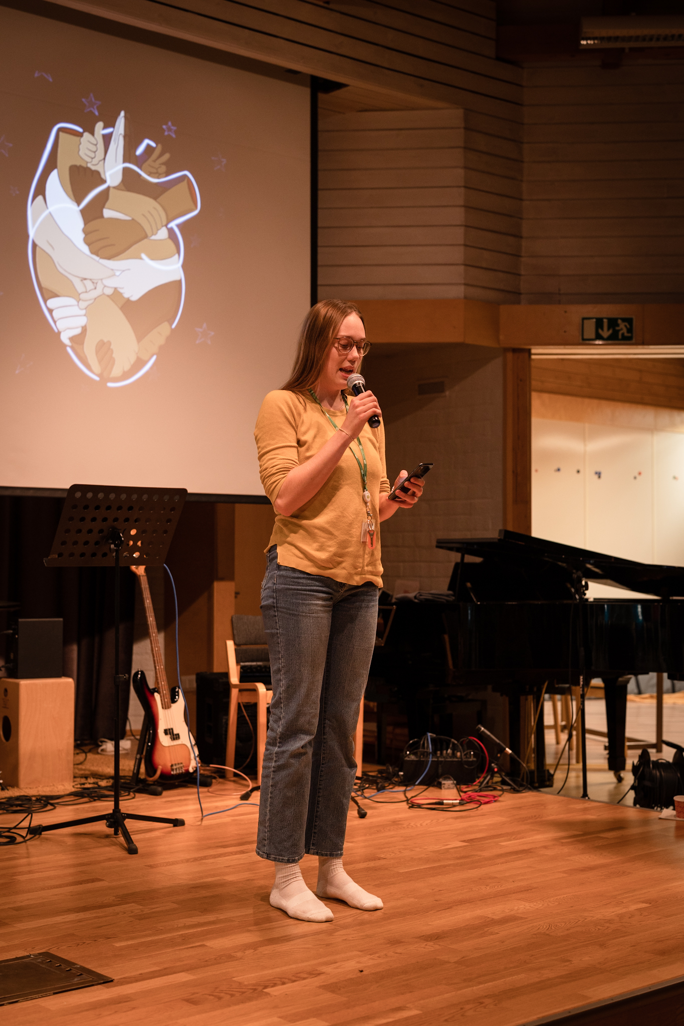 Ung kvinna med långt hår, ljus skjorta och jeans läser en dikt i mikrofon på en scen.