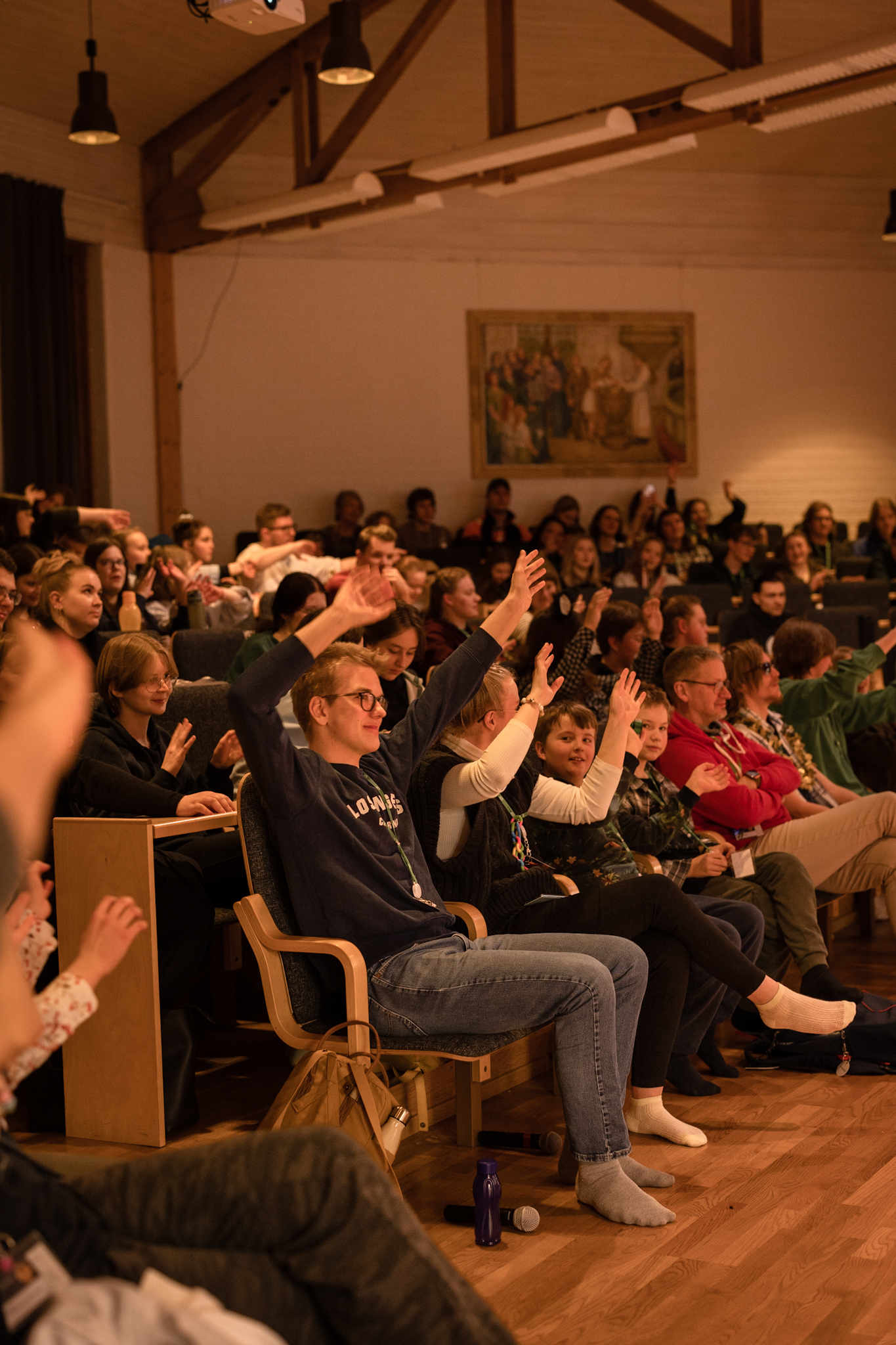Ungdomar och vuxna i ett auditorium klappar i händerna åt ett program.