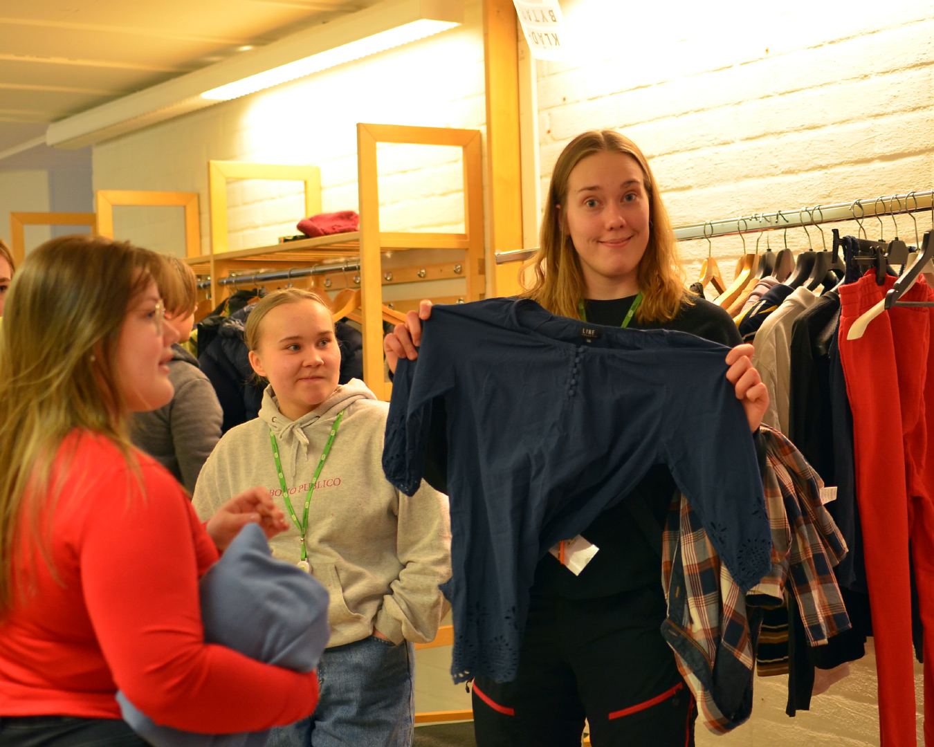 En ung kvinna håller upp en mörkblå skjorta. Två andra står på sidan om och tittar.