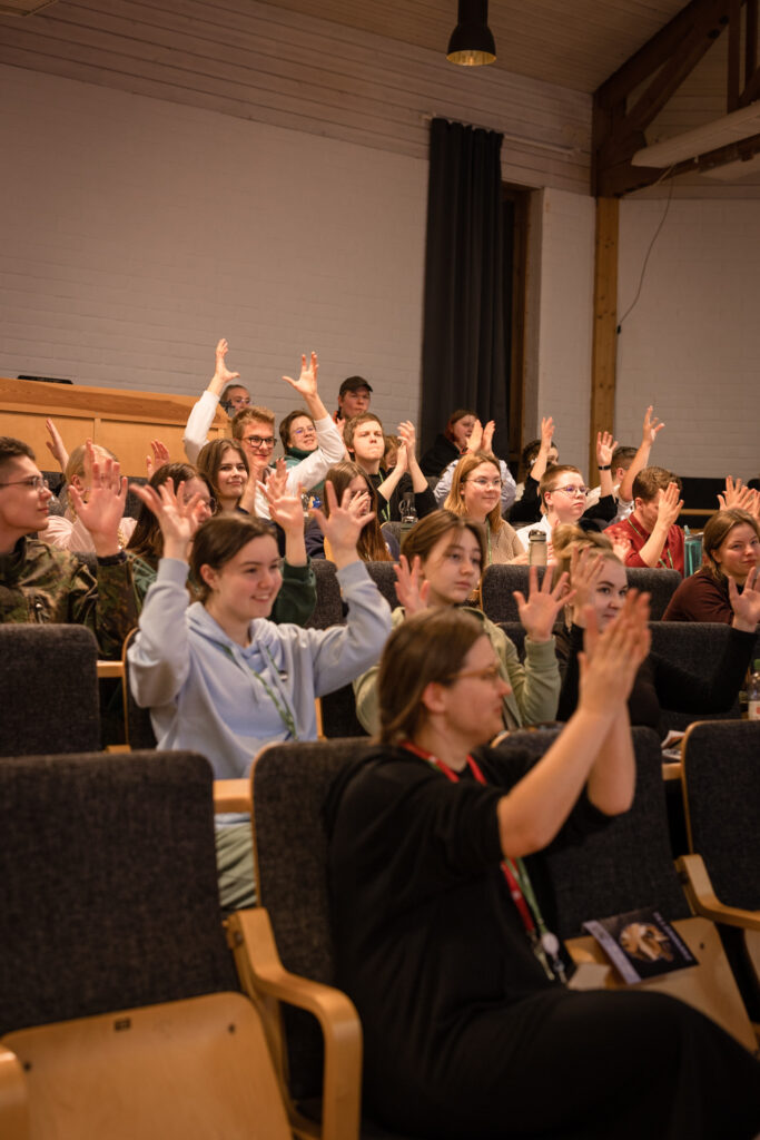 Ungdomar sitter i ett auditorium och applåderar på teckenspråk