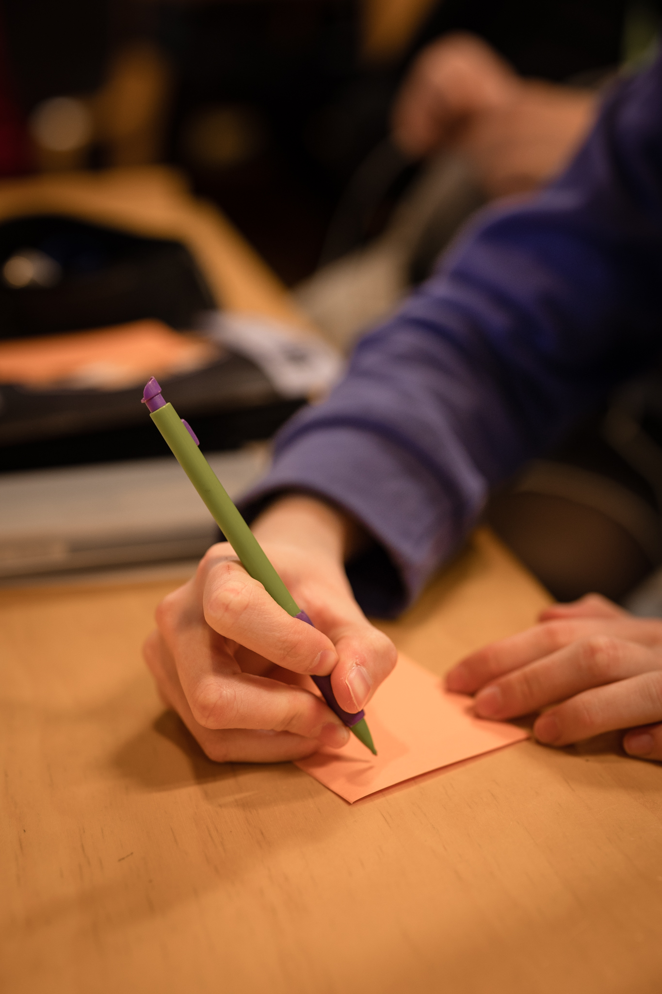 En hand håller i en penna och skriver på en orange lapp.