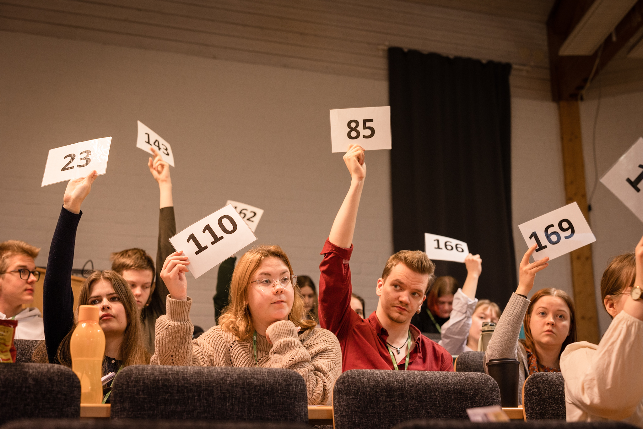 Ungdomar sitter i ett auditorium och håller upp sifferkort.