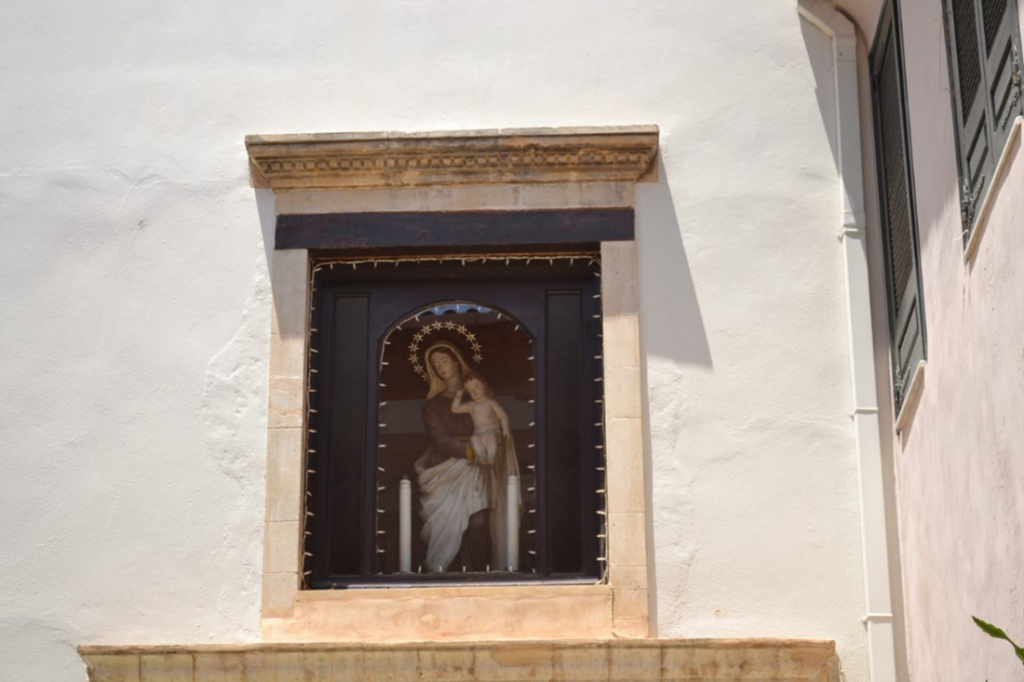 I fönstret på ett vitrappat hus sitter en Maria-figur.
