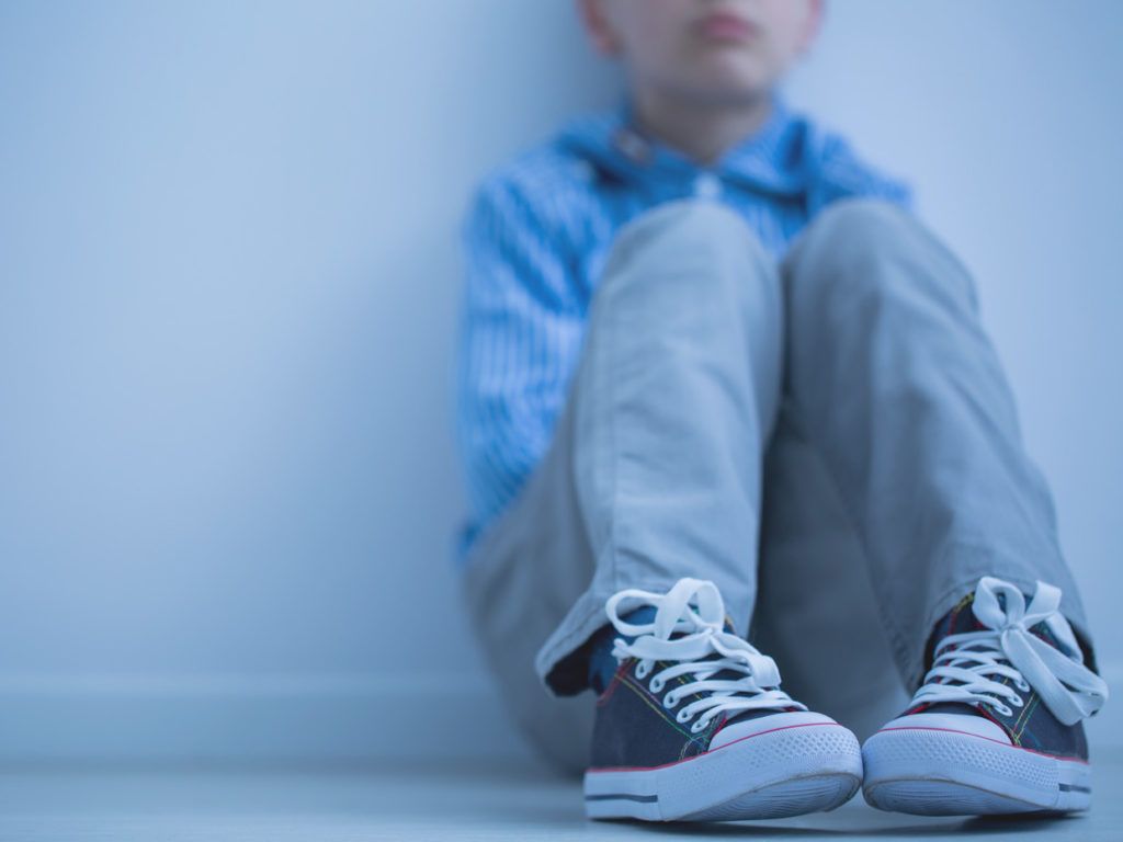 Ett barn sitter lutad mot väggen med knän uppdragna mot famnen.
