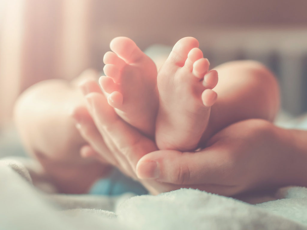 En vuxen hand kupad under ett par små babyfötter.