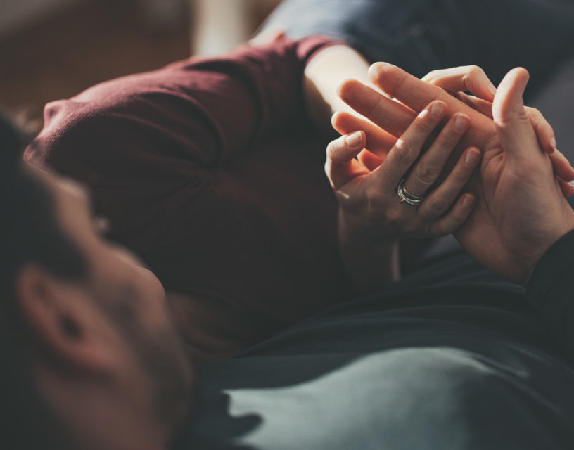 Par ligger tillsammans i en soffa, bilden fokuserar på deras händer.